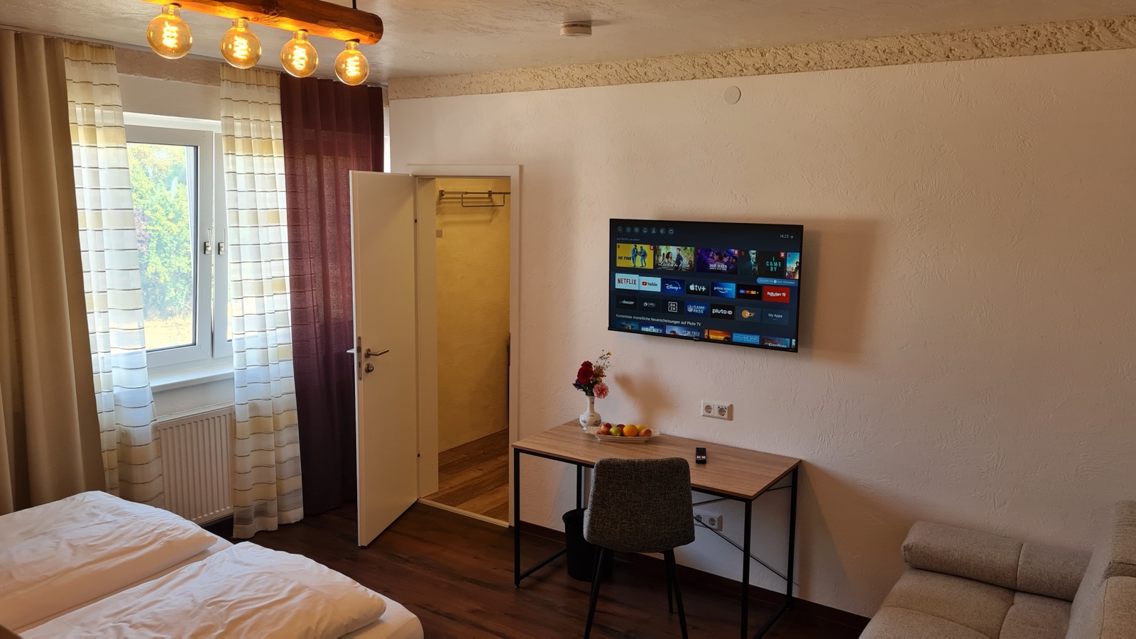 Wohnbereich mit Schreibtisch, Fernseher und Fenster in Zimmer 5