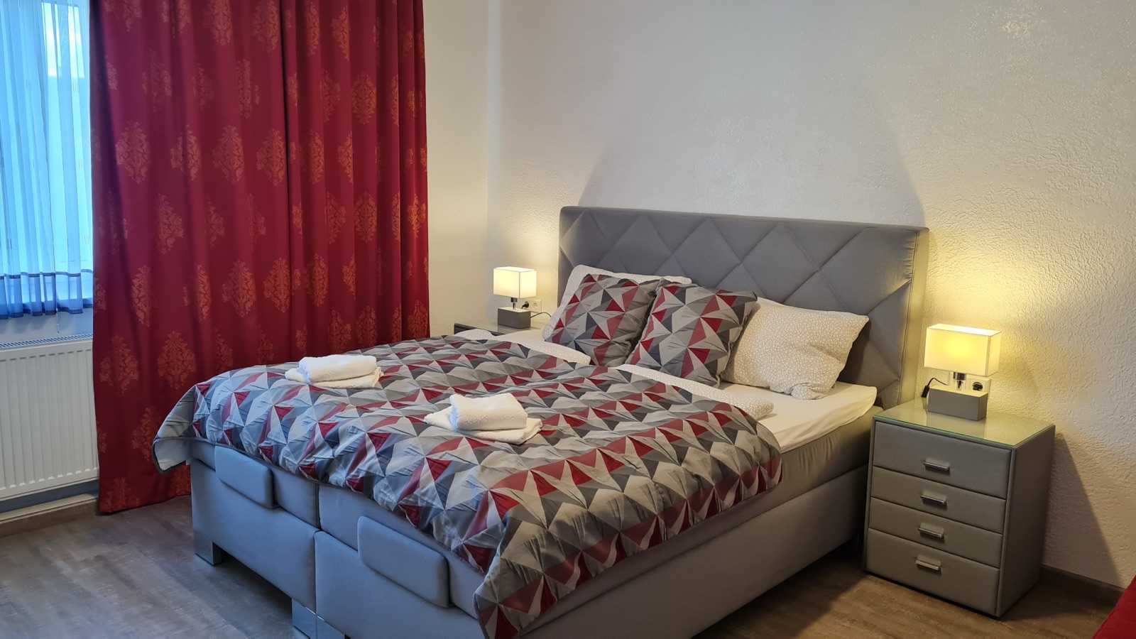 Bett mit gemusterter Bettwäsche und roten Vorhängen in Zimmer 7